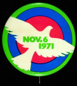 Vietnam War protest button picturing red, blue, and green rings behind a white outline of a bird. "Nov. 6 1971" is printed in green.