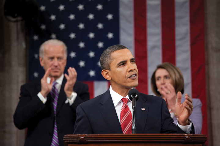 President Barak Obama giving a speech. Behind him is Joe Biden and Nancy Pelosi