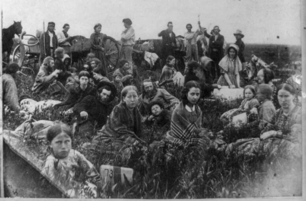 "People escaping from the Indian massacre of 1862 in Minnesota, at dinner on a prairie". Photo shows the U.S.-Dakota War of 1862. Right half of stereograph published by Whitney's Gallery, St. Paul, Minn. This photo is actually Mixed Bloods who were rescued by non hostile Indians. The girl in the foreground wrapped in the striped blanket is Elise Robertson, the sister of Thomas Robertson a mixed blood who acted as a intermediary between the hostile and non hostile Indians and the whites.