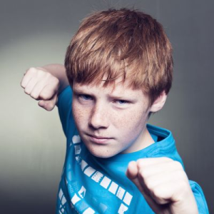 A child with red hair and freckles making a fist, looking menacingly at the camera