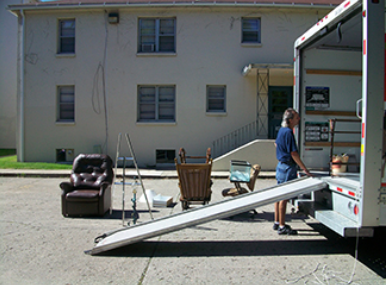 A person stands outside a moving truck with their belongings around them.