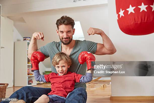 A young boy poses in boxing gloves with arms raised in a "Hulk" pose with an older man doing the same.