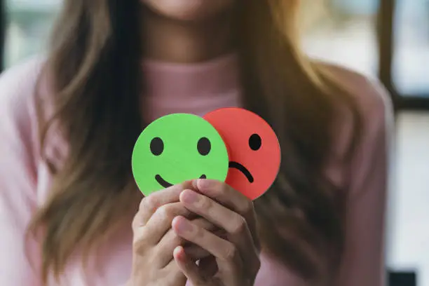 A person holding a smiley face and sad face