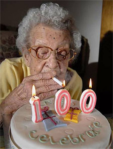 An old person lighting a cigarette on a birthday cake celebrating 100 years old