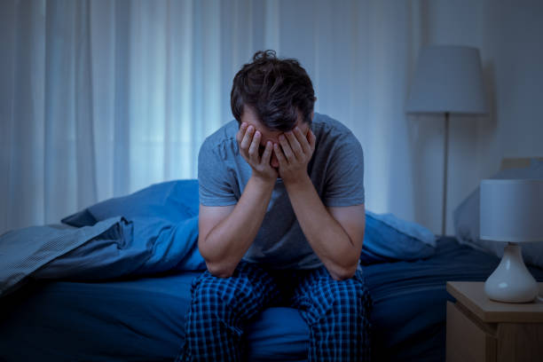 A person sitting on a bed with his hands in his face