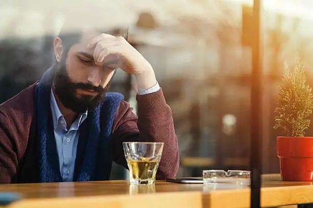 A person with his hand on his head looking at a shot of liquor in front of him.