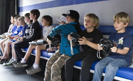 A group of kids sitting on a bench, all looking in the same direction and not at each other, holding video game controllers.