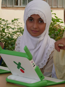 A young Iraqi child wearing a white head scarf with a laptop