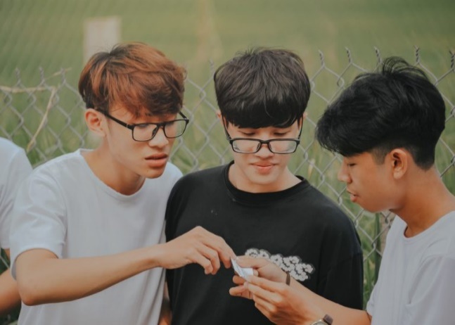 A group of young men standing outside looking at something puzzling together.