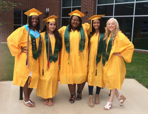 Five young adult women stand in graduation robes, hats and tassels smiling for the picture.