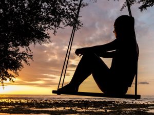 woman on a swing looking toward the sunset