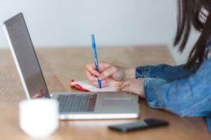 woman writing on paper with a laptop nearby