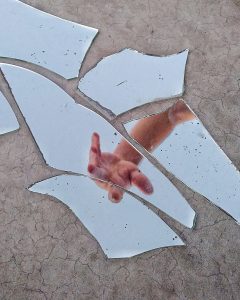 a hand seen in cracked shards of a mirror on the ground