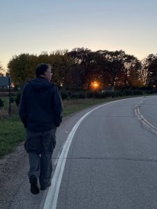 Man walking down a road that curves with a sun set