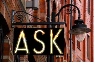 A sign stating, "ASK" next to a lamp post.