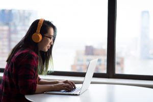 woman listening to headphones and typing on her computer