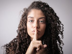 woman with ring finger to her mouth in a "shhh" symbol.